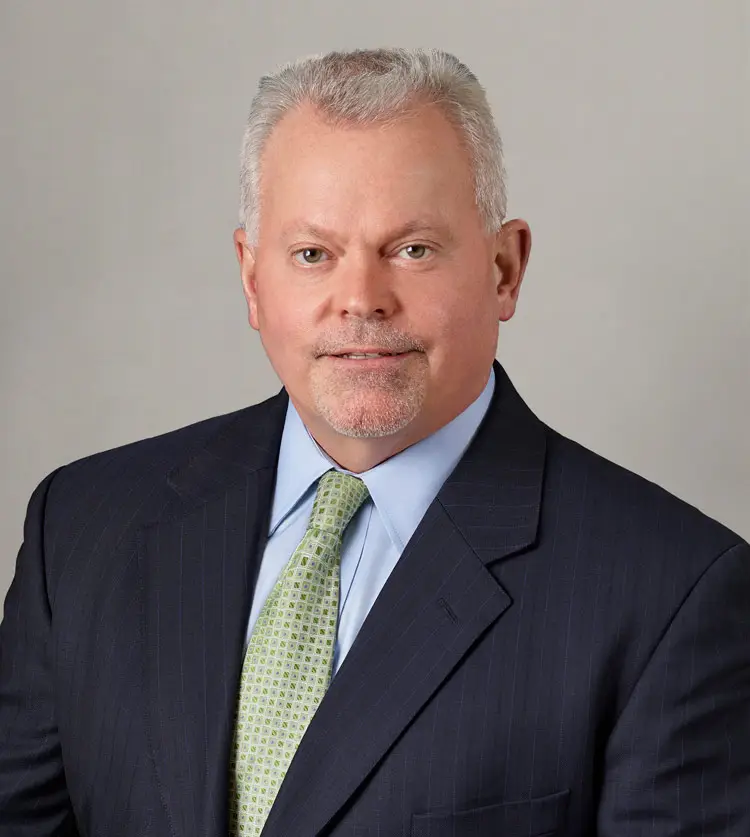 A flight school finance professional in a navy suit and green tie posing against a gray background.
